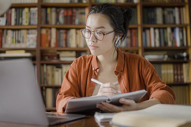 Young woman student taking online course, sitting with laptop in the library