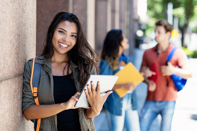 Laughing mexican student with tablet computer and friends in background in front of university building