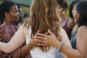 Diverse group of women standing arm in arm together in a circle during an outdoor session at a wellness retreat in summer